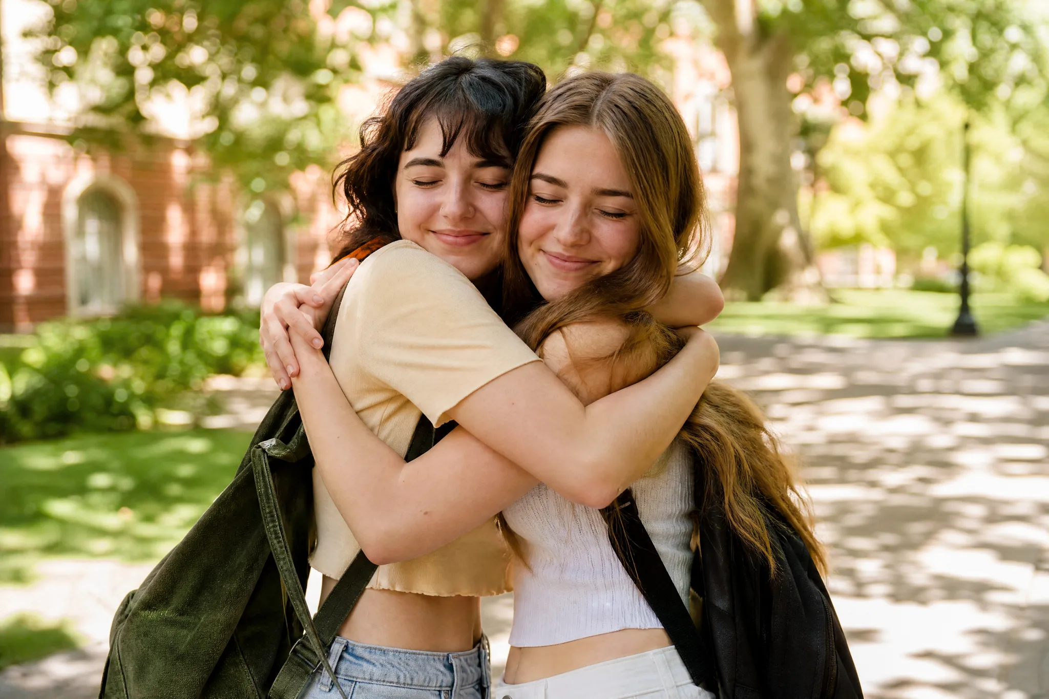 AI Hugging Video: Two Photos into One Hug Two young women with eyes closed in a big warm hug on a sunlit walkway under green trees