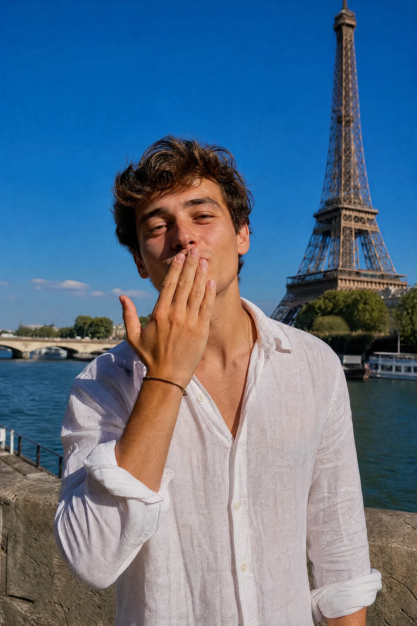 The Air Kiss by the Eiffel Tower Young man raising his fingers to his lips to blow a kiss on a sunny Paris riverside with the Eiffel Tower behind