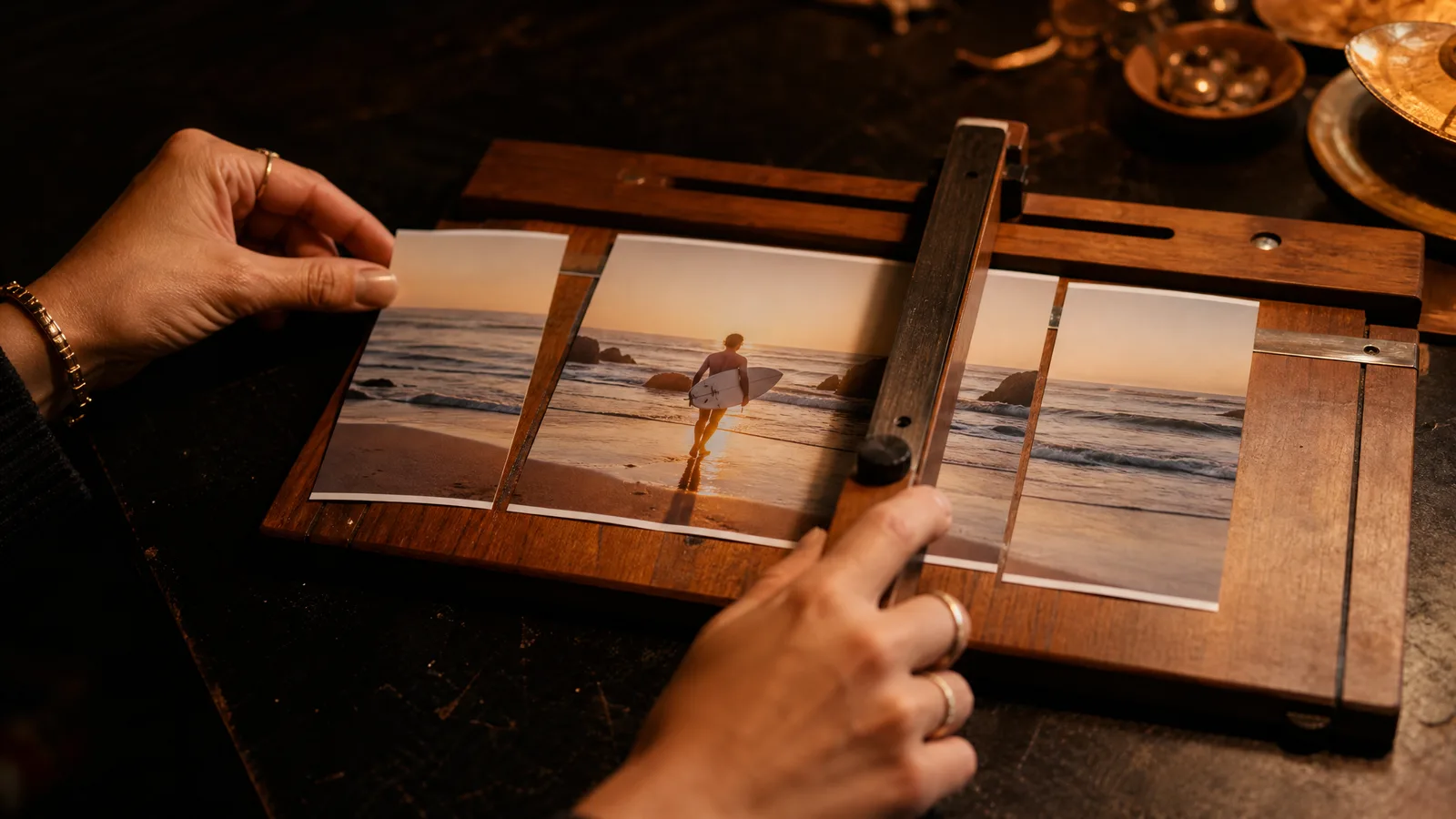 Hands trimming a wide beach photo print into a tall vertical strip centred on a surfer with a paper trimmer