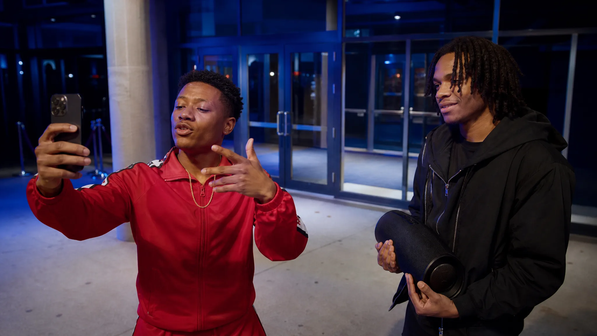 Bulin 47 AI Template: A Styling Note Performer in a red tracksuit and gold chain freestyling at a venue entrance under cool blue light as a friend holds a speaker