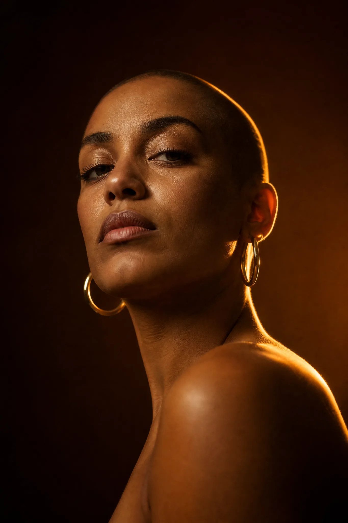 Grok Imagine Image: Mood Through Light Woman with a shaved head and gold hoops in warm rim light from a low viewpoint