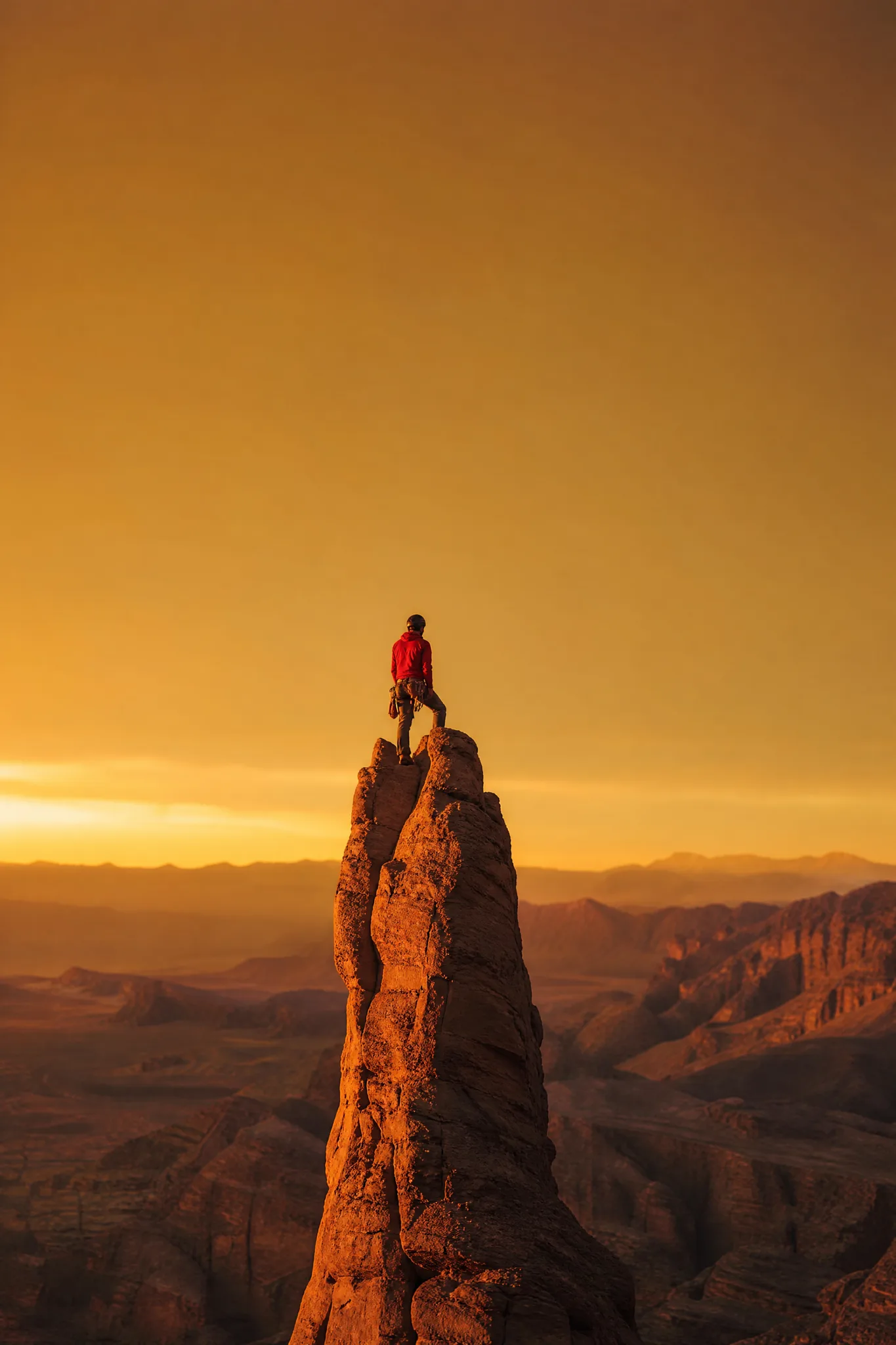 Grok Imagine Image: Composed for the Project Climber in a red jacket on top of a slender sandstone tower with wide open sky above
