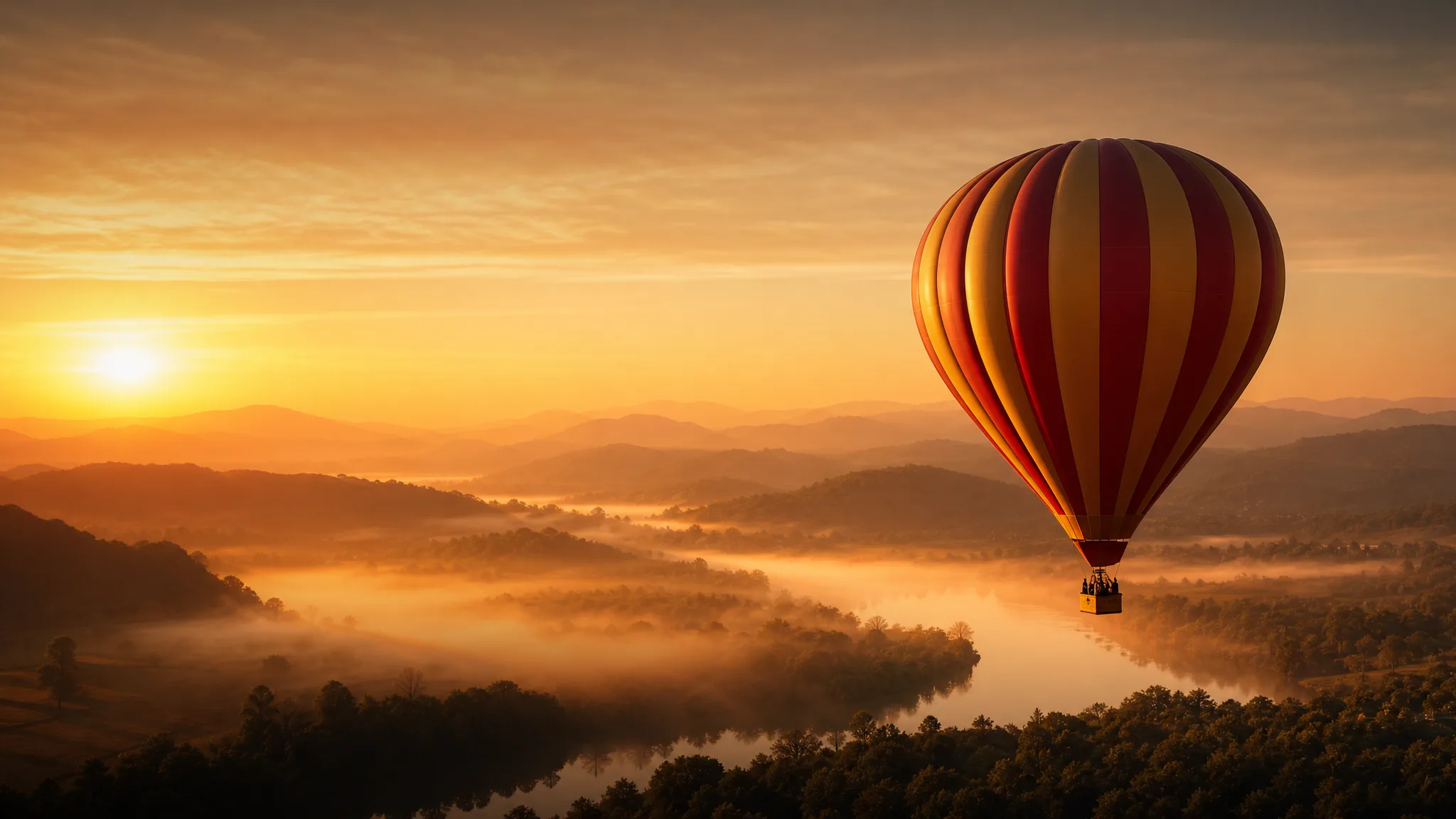 Red and gold hot-air balloon drifting over a misty river valley at sunrise with open sky beside it