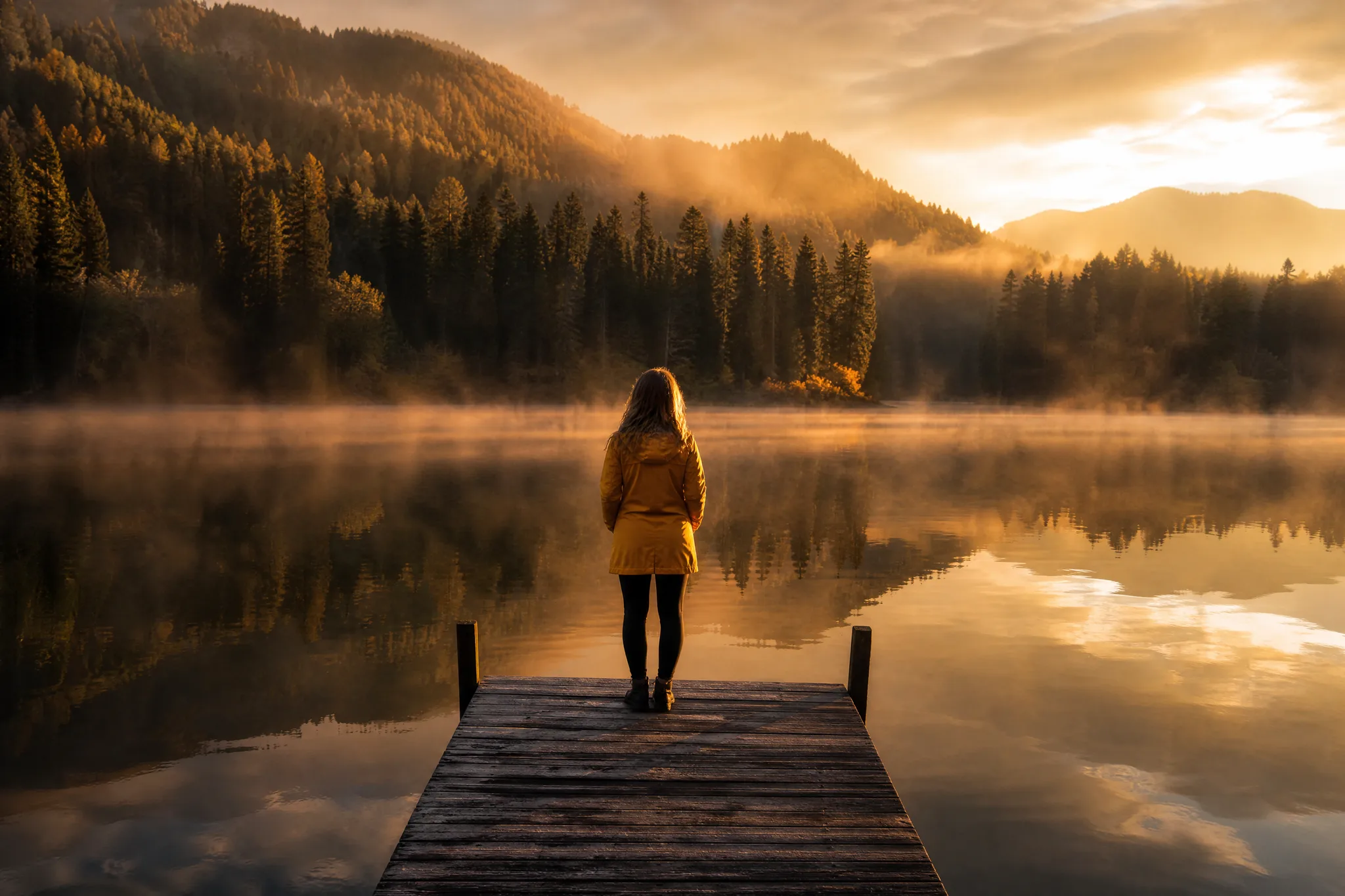 Veo Image to Video: Mist over a Lake at Dawn Woman in a yellow rain jacket standing at the end of a wooden dock on a misty lake at dawn